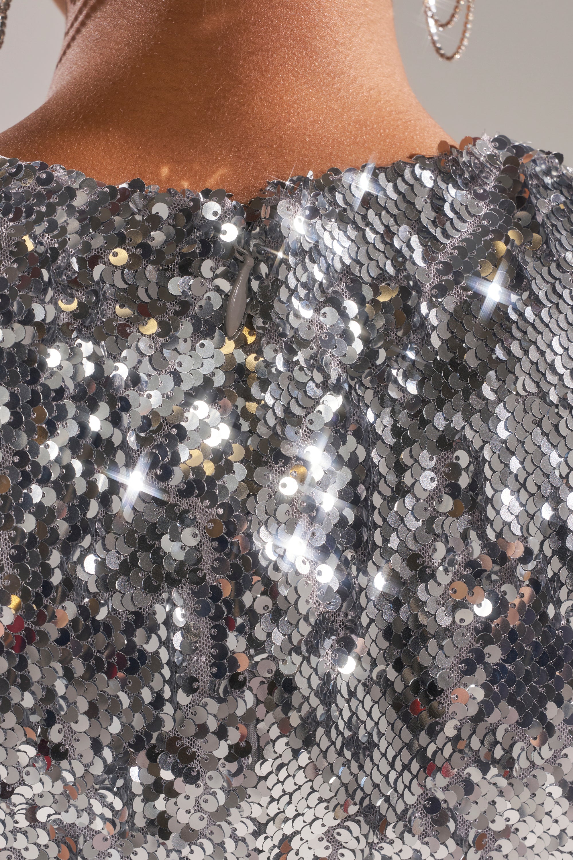 Close-up of the back of a person wearing the DANCE THE NIGHT AWAY SEQUIN MINI DRESS IN SILVER, featuring shiny, reflective sequins that catch the light. A hoop earring and part of the neck are also visible—perfect for any party look.