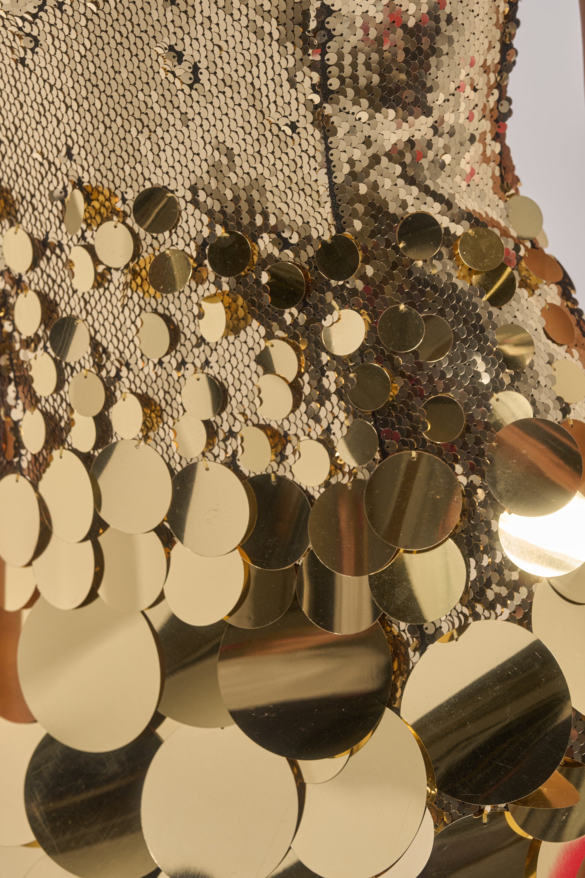Close-up of reflective gold sequins and metallic discs on fabric, creating a textured, shimmering look—ideal for the DANCE THE NIGHT AWAY SEQUIN MINI DRESS IN GOLD, perfect for making a statement at any party.