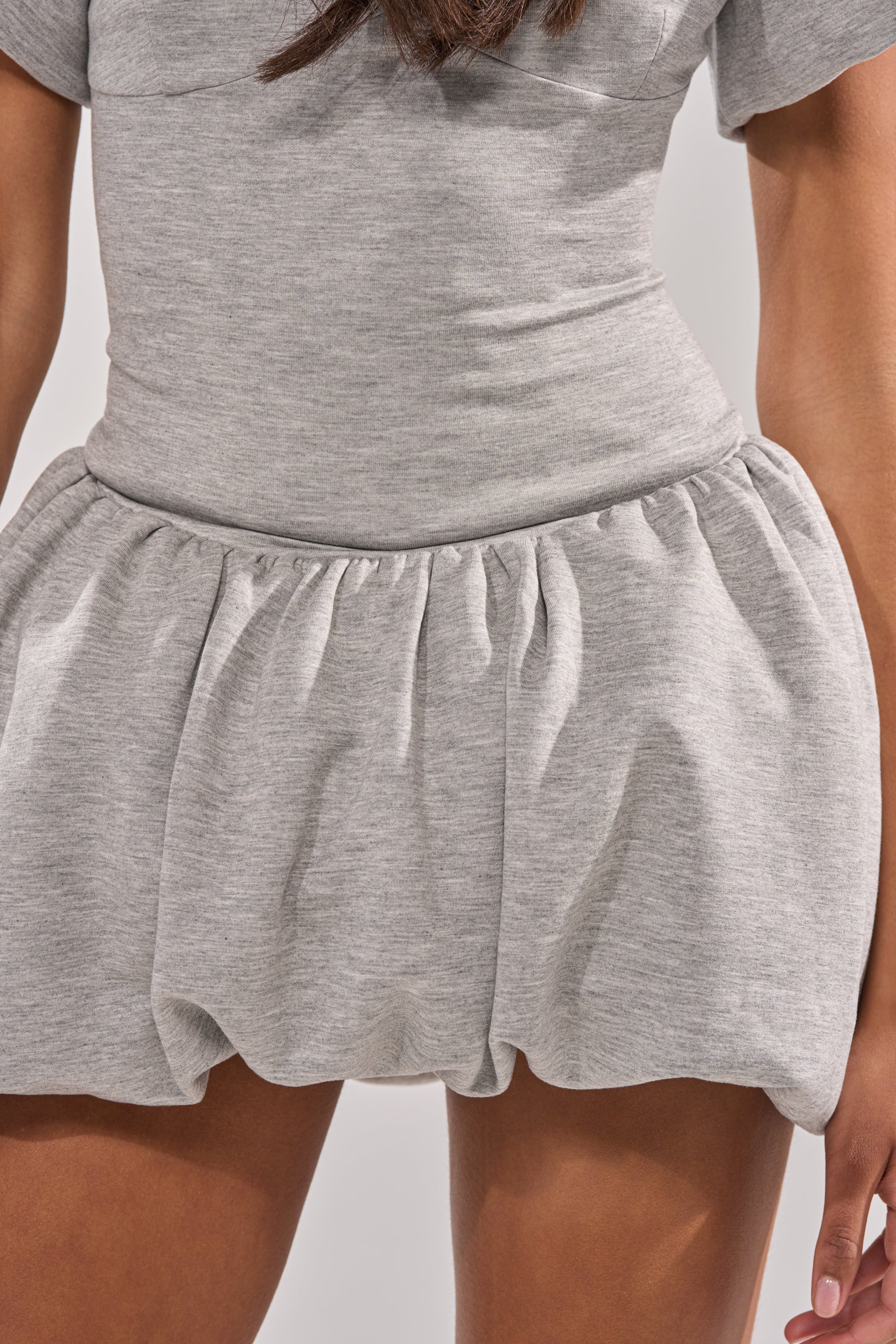 A person wears the GIRL POWER FRENCH TERRY MINI DRESS, a light gray streetwear piece featuring short sleeves, a fitted bodice, and a puffy gathered skirt. The image shows the outfit from waist to mid-thigh. 8