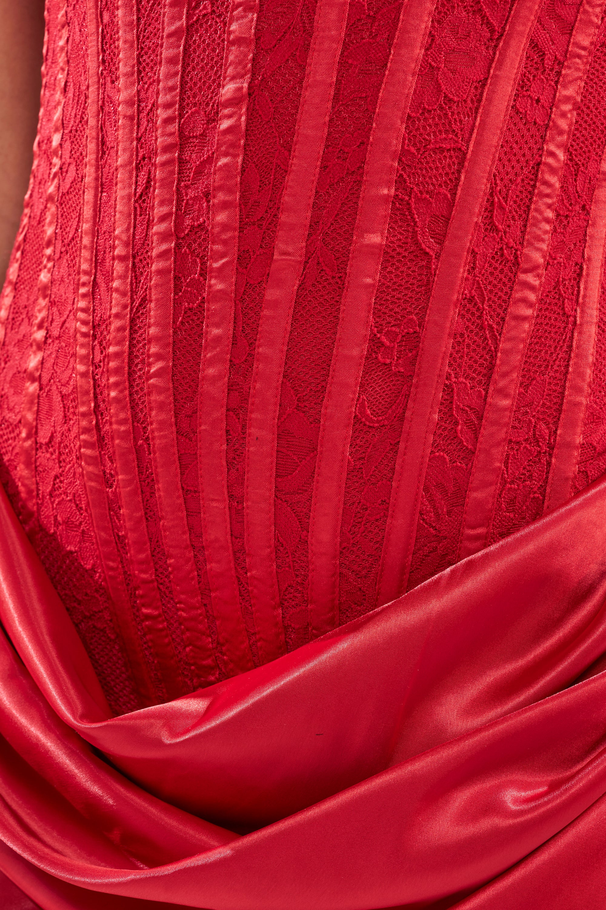 Close-up of the SPOIL ME LACE MINI DRESS IN RED, showcasing vertical lace and satin panel details with gathered, shiny satin fabric draped along the hem.