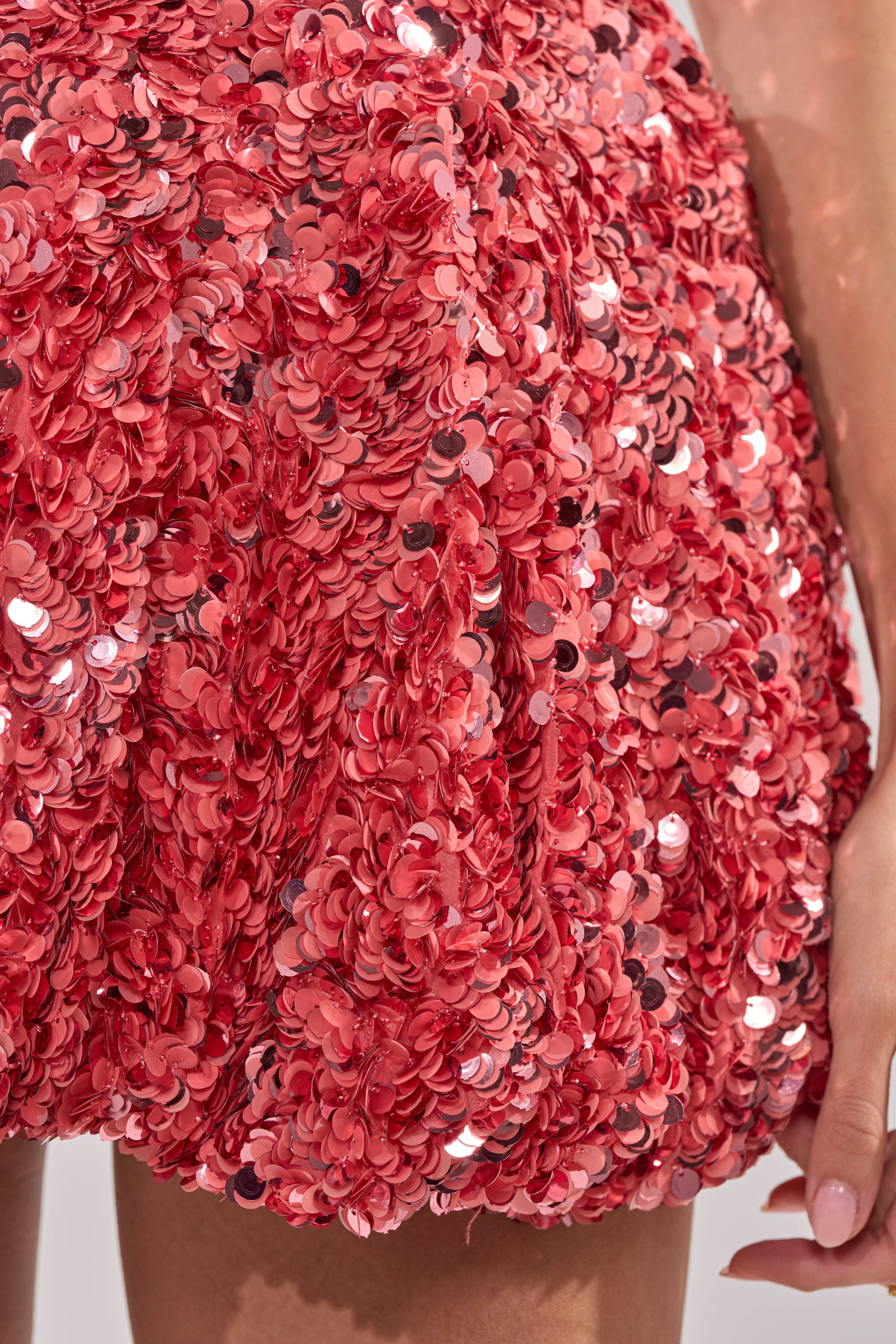 Close-up of a hand next to the BARBIE GIRL SEQUIN MINI DRESS in pink, featuring shiny sequins and floral embellishments for a sparkling, three-dimensional look.