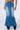 A person modeling the RICH GIRL ENERGY EMBELLISHED DENIM MAXI SKIRT adorned with tiny silver studs. This full-length denim skirt features a slight flare at the hem, faded sections along the front, and five-pocket styling. The model is also wearing black heeled boots.