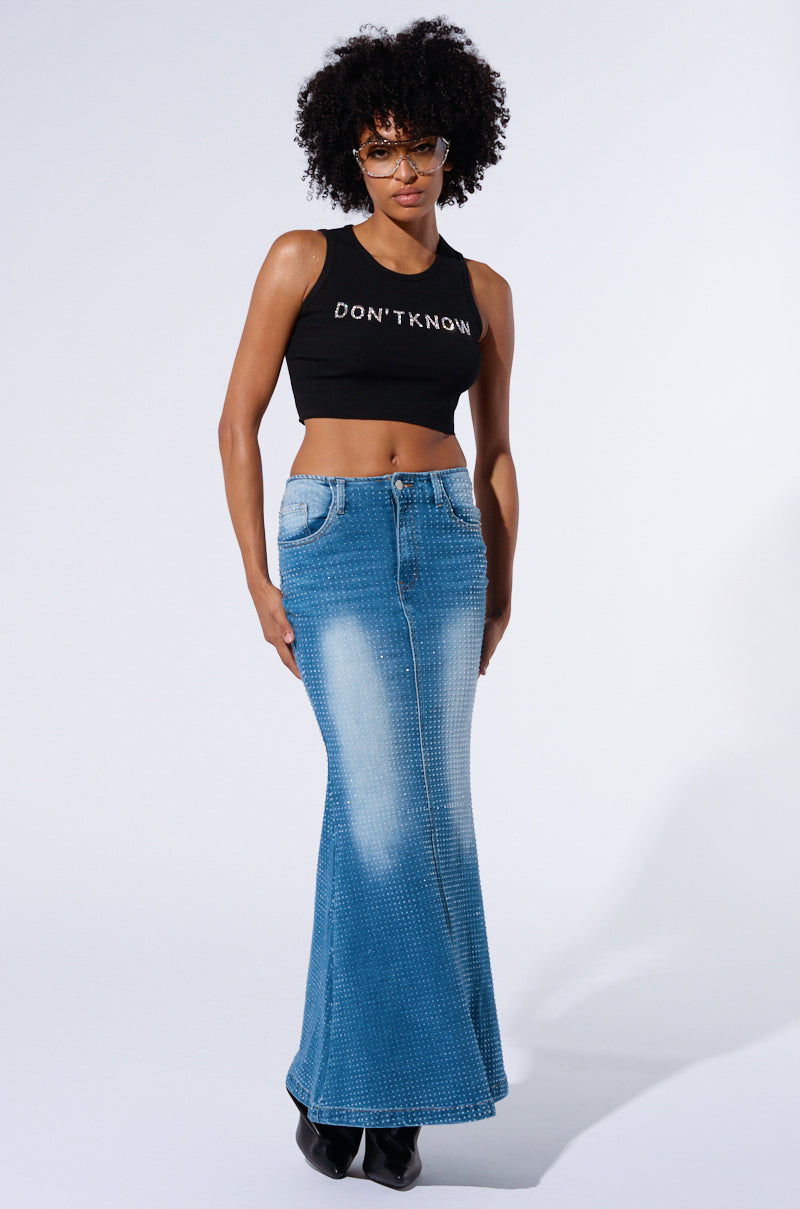 A person with curly hair, wearing glasses, a black sleeveless top with the words "DON'T KNOW" printed on it, and the RICH GIRL ENERGY EMBELLISHED DENIM MAXI SKIRT stands against a plain white background. They are looking directly at the camera.