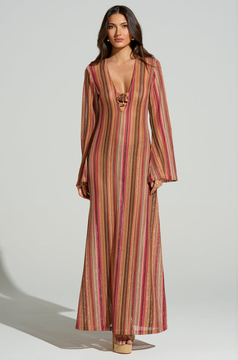 Someone is wearing the IBIZA DREAMIN CROCHET MAXI DRESS, a long, striped dress in earthy red, brown, and beige tones, featuring a low crochet knit neckline. They're standing on a plain backdrop and wearing summer vibe platform sandals.
