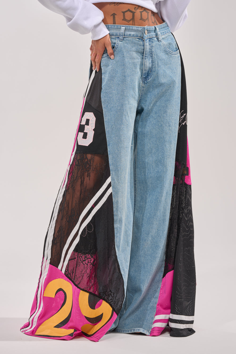 Someone in the GAME TIME RELAXED DENIM: high-waisted, wide-leg jeans with black, pink, and yellow mesh sports jersey panels—numbers 29 and 3—and white stripes overlaid for a bold streetwear look. 1