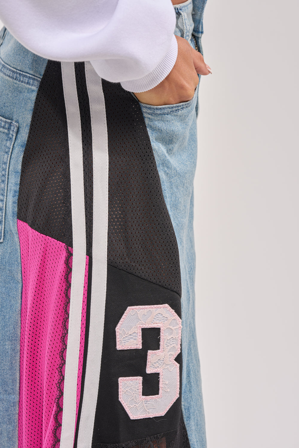 Wearing the GAME TIME RELAXED DENIM—light blue jeans with black mesh, pink fabric, white stripes, and a bold "3"—paired with a white long-sleeve top, they strike an effortless streetwear vibe with a hand casually in the pocket. 8