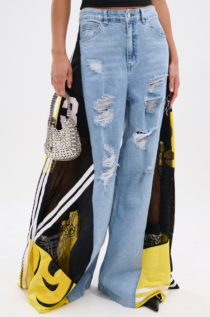 Only the lower torso and legs are visible, dressed in DONT MESS WITH ME WIDE LEG DENIM PANT—high-rise, wide leg light blue denim with ripped details and black/yellow fabric panels—paired with a small silver handbag.