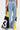 A person faces away wearing the DONT MESS WITH ME WIDE LEG DENIM PANT, which features high-rise fit, wide legs, and patchwork panels in yellow, black, and sheer number-print sections. They hold a small silver handbag in their right hand.