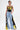 Wearing the DONT MESS WITH ME WIDE LEG DENIM PANT, light blue with yellow and black panels, and a black halter top with a yellow “79,” this confident individual accessorizes with a small silver purse and sports short, styled hair.