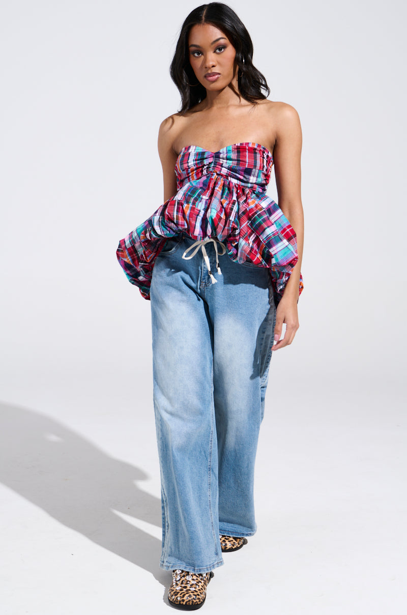 A person confidently walks toward the camera against a plain backdrop, wearing a vibrant Y2K-inspired Mixed Plaid Cropped Bubble Blouse and light blue wide-leg jeans, paired with leopard print shoes.