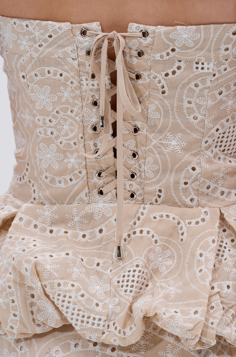 Close-up of the back of the SUMMER TIME BLISS EYELET CORSET dress in beige, showcasing white embroidered eyelets, a lace-up back with beige laces through metal eyelets, and a ruffled waist hem. 7