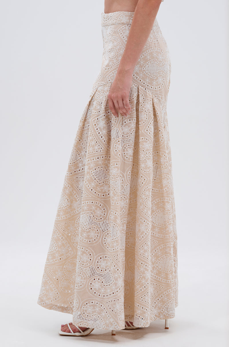 A woman showcases the SUMMER TIME BLISS EYELET TROUSER, a cream-colored, ankle-length piece with paisley-patterned eyelet lace, styled with open-toe heels and seen from the side against a plain backdrop. 3