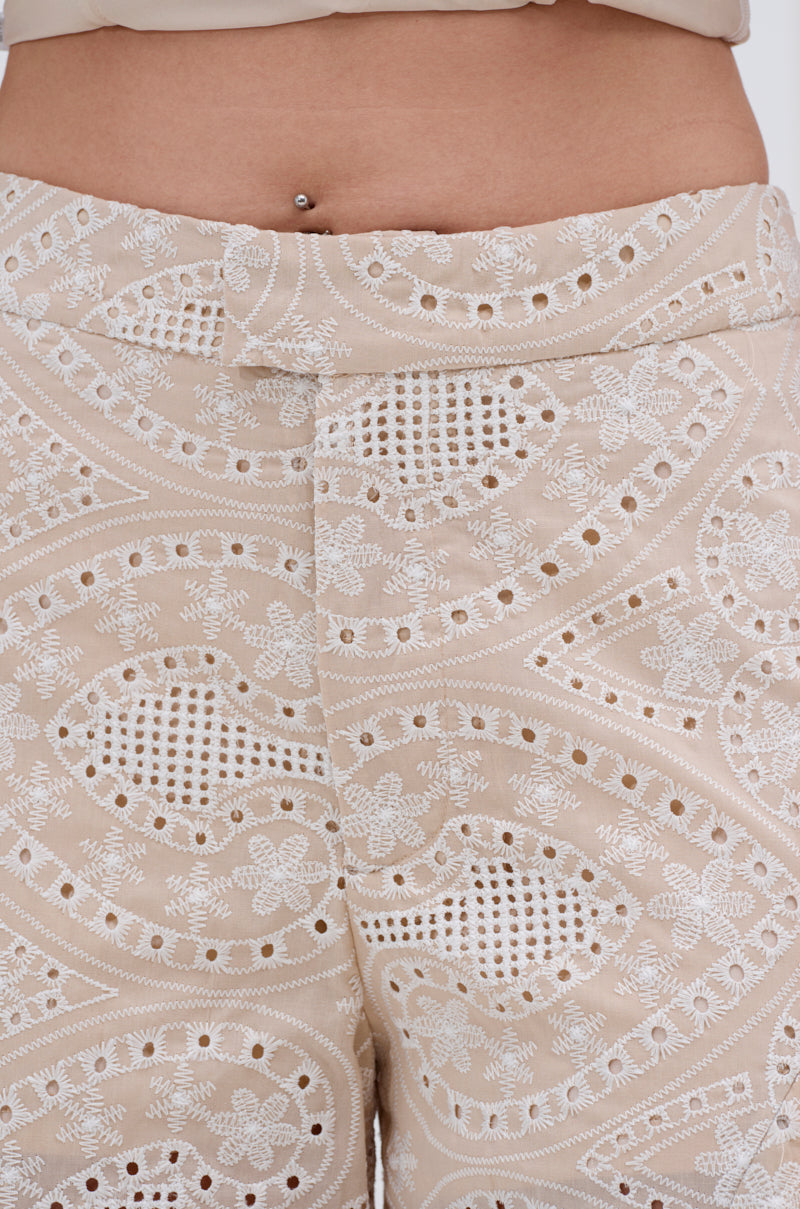 Close-up of the SUMMER TIME BLISS EYELET TROUSER in beige, featuring intricate white lace embroidery and cut-out patterns. The wearer’s belly button piercing adds to the carefree summer vibe. 6