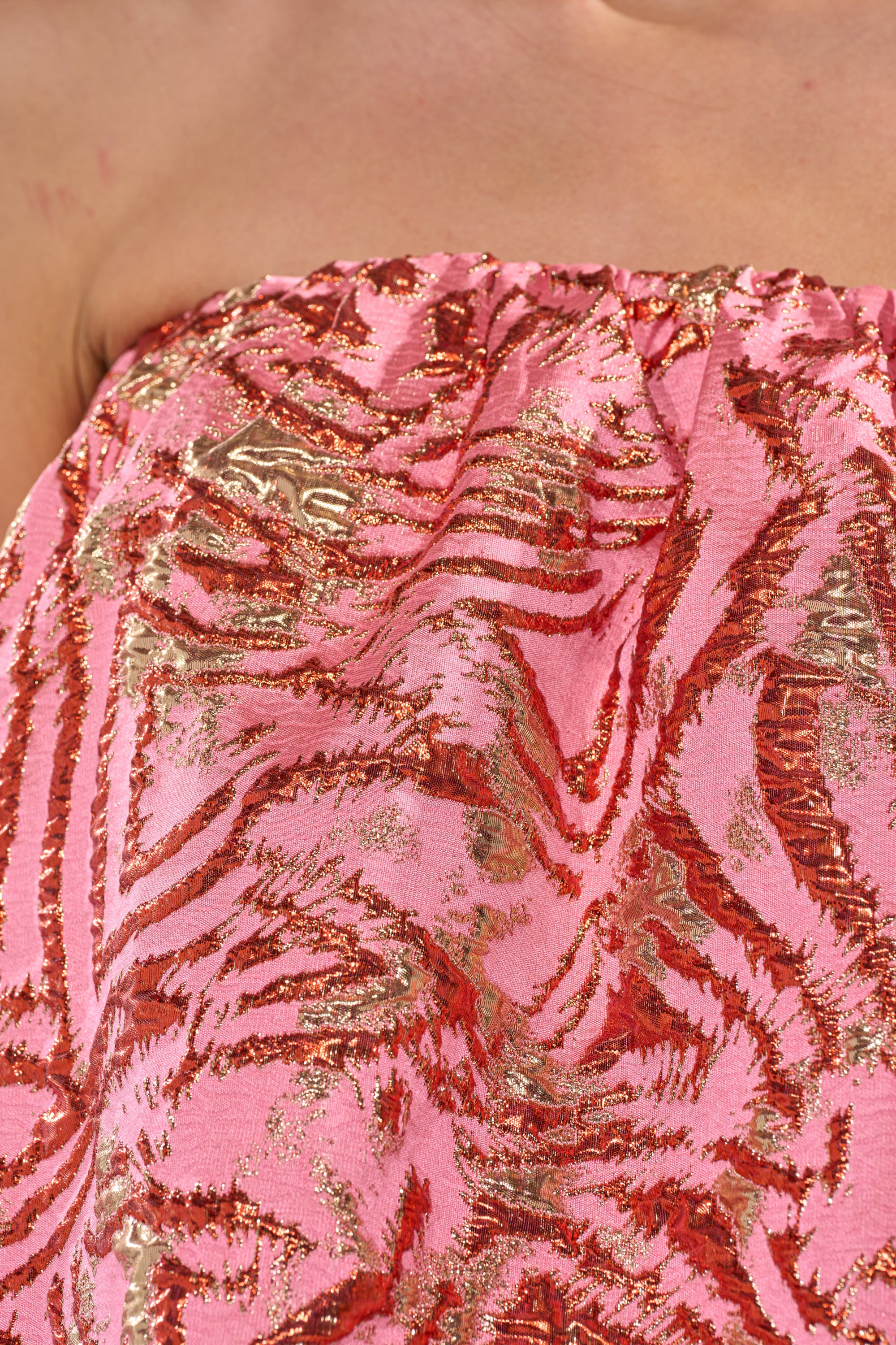 A close-up of a person's upper chest and shoulders wearing the LOVER GIRL BROCADE BUBBLE DRESS IN PINK, a strapless mini dress featuring a shiny, textured zebra pattern. 6