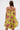 A woman with long, straight brown hair is shown from the back wearing the LOVER GIRL BROCADE BUBBLE DRESS, a couture-inspired strapless yellow dress with a pink and green floral pattern. The background is plain white.