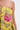 A close-up of someone in the LOVER GIRL BROCADE BUBBLE DRESS, a couture-inspired strapless yellow piece with textured pink and metallic floral embroidery, set against a plain white background.