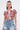 A woman wears large angular earrings and the BEACHY BLISS CROCHET SHORT SLEEVE BUTTON DOWN, featuring a lavender collar and zigzag pattern, paired with high-waisted, belted denim shorts against a plain white background.