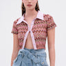 A woman wears large angular earrings and the BEACHY BLISS CROCHET SHORT SLEEVE BUTTON DOWN, featuring a lavender collar and zigzag pattern, paired with high-waisted, belted denim shorts against a plain white background.
