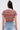 A person with long brown hair, seen from the back, wears the BEACHY BLISS CROCHET SHORT SLEEVE BUTTON DOWN and light blue jeans. An insulin patch is visible on their upper left arm against a plain, light background.