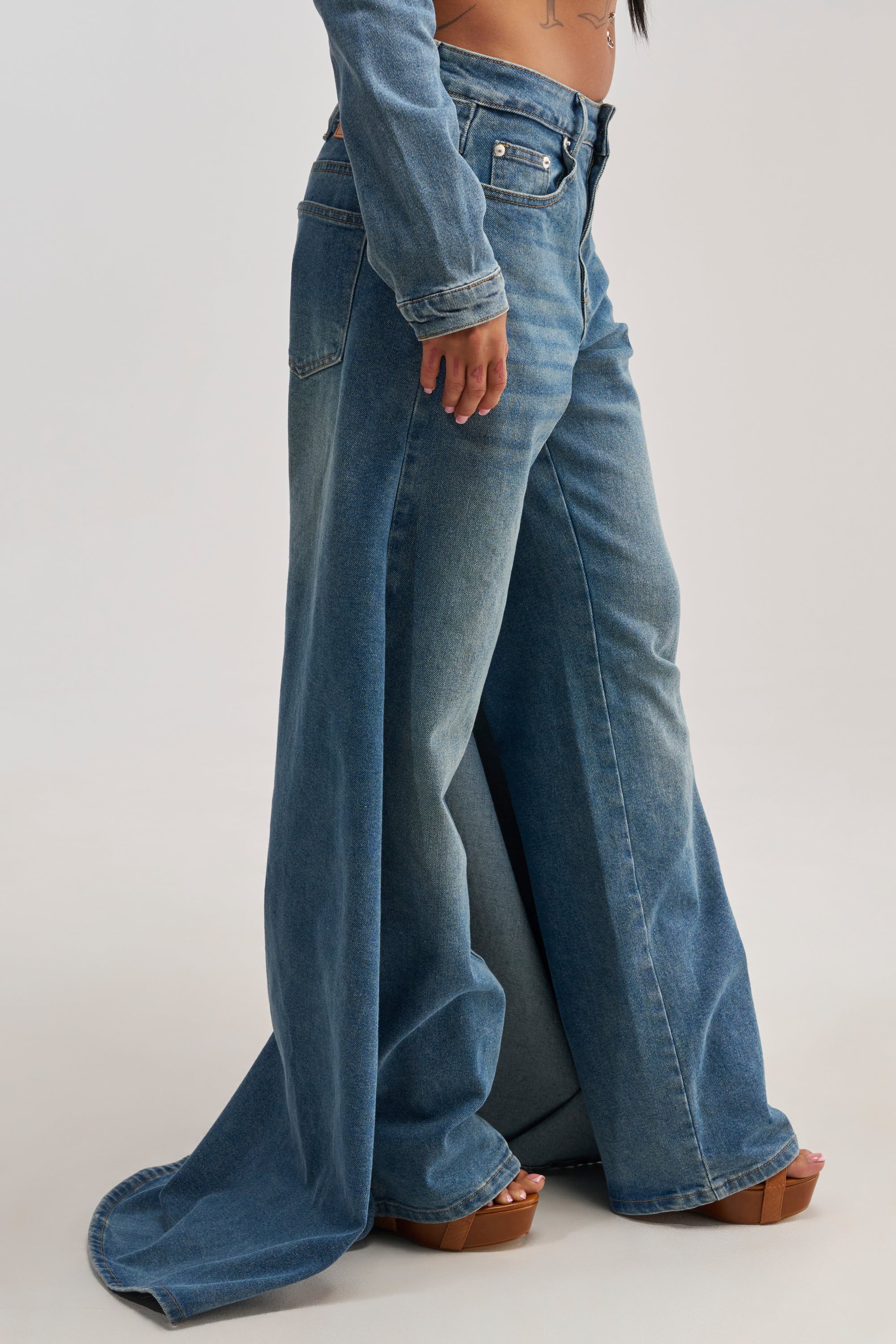 A person wearing the SHAKE IT OFF DENIM PANT WITH SKIRT ATTACHED and brown platform sandals, standing on a light background.