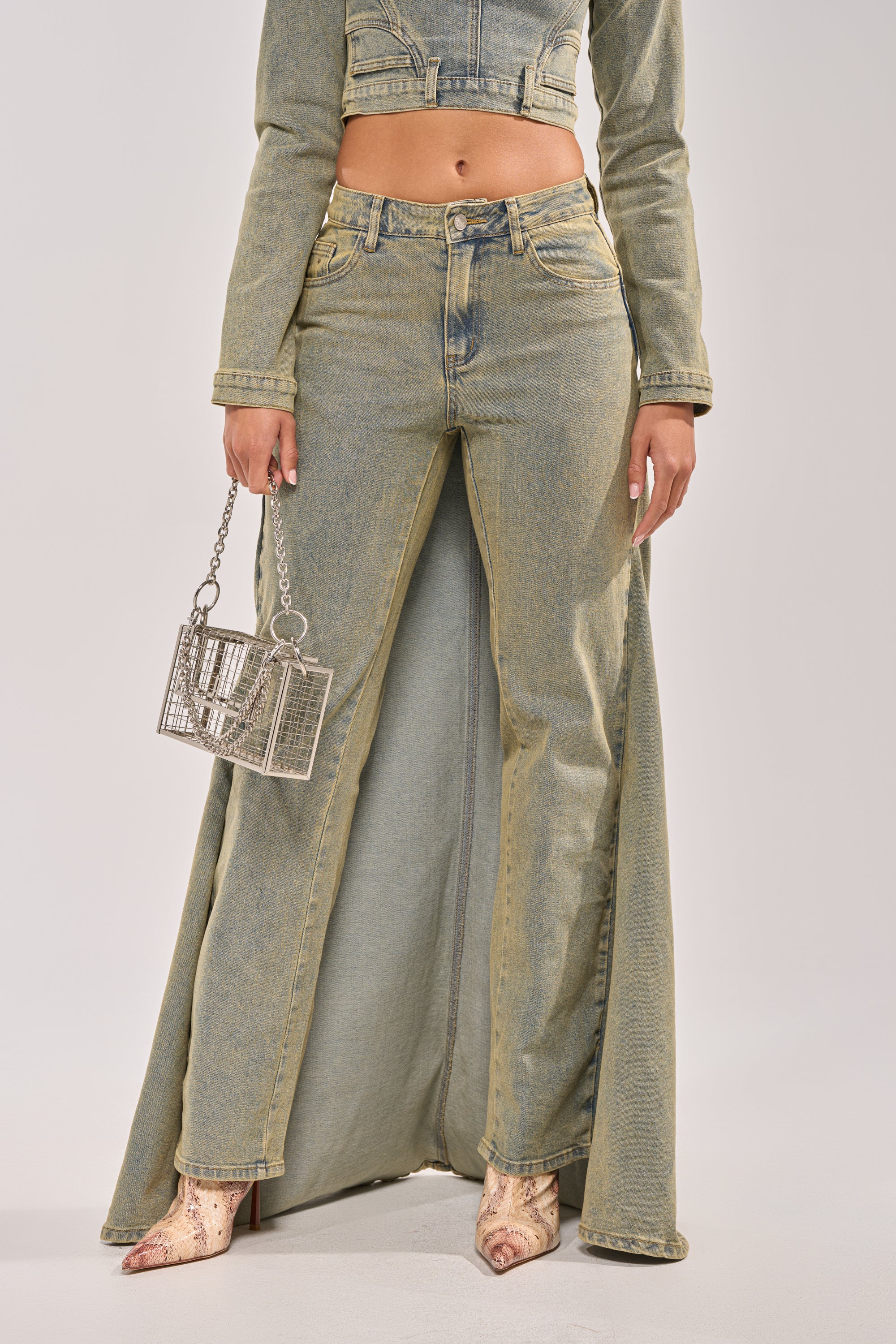 A person in BIG STEPPER DENIM PANTS with a matching denim jacket, metallic mini handbag, and pointed snakeskin-print shoes. Image cropped at the shoulders. 1