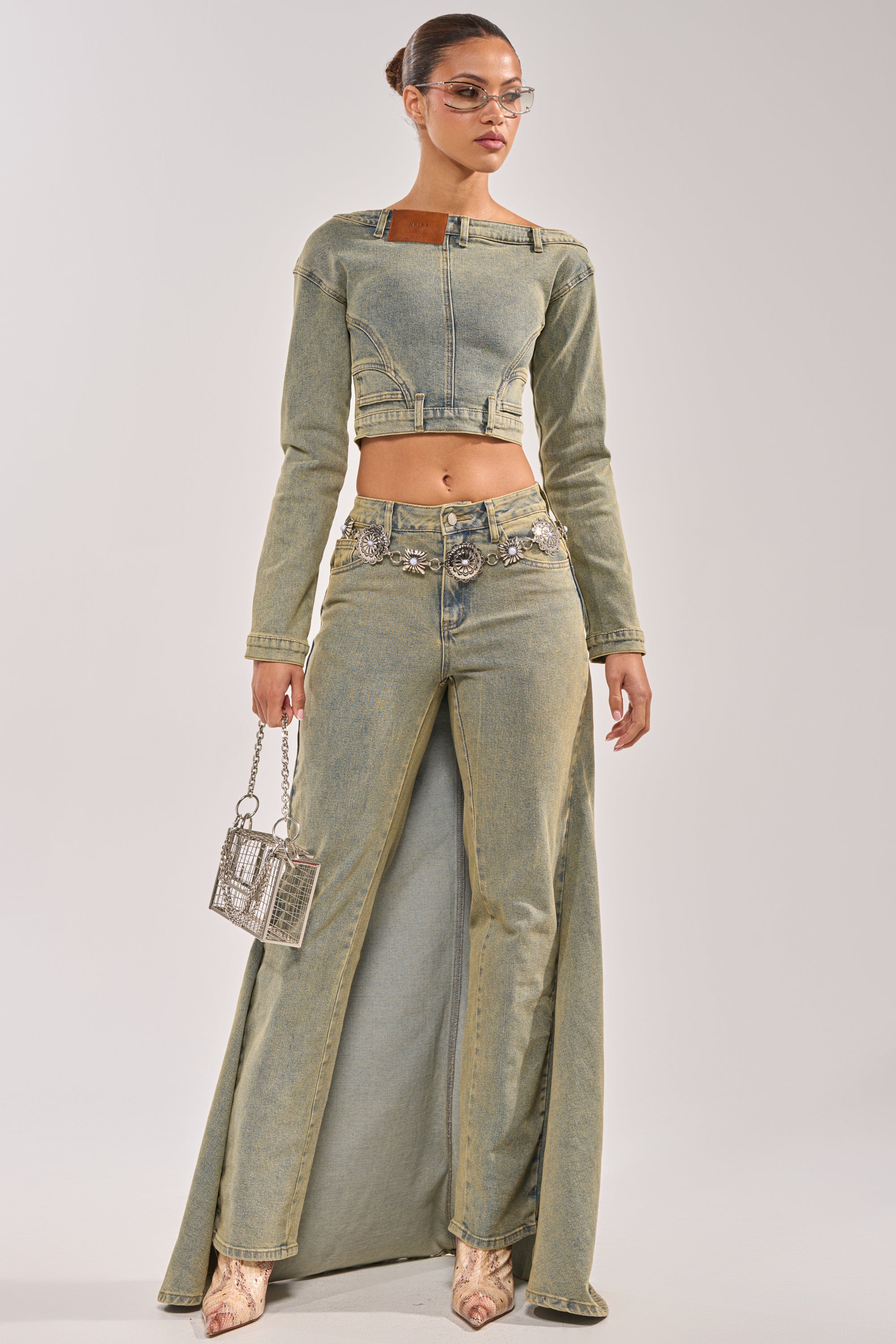 A woman wears the BIG STEPPER DENIM PANT with a light denim crop top, pairing it with a metallic square handbag, sunglasses, and a sleek bun. 5