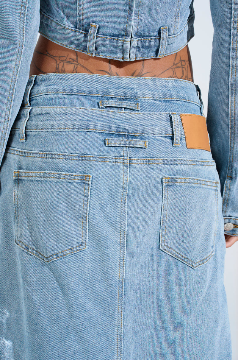 A person is shown from the back wearing SHAKE IT OFF DENIM PANT WITH SKIRT ATTACHED, featuring blue denim with visible seams, pockets, and a brown waistband patch. Tattoos accentuate the lower back.