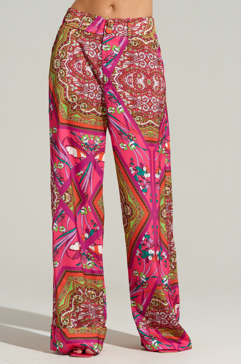 The MOVE AND SHAKE TROUSER IN PINK MULTI showcases a pair of wide-leg pants featuring a vibrant pink, orange, and brown paisley pattern. These trousers skillfully combine floral motifs with intricate geometric designs for a striking silhouette.