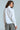 A person with long hair wears a crisp BOSS ENERGY BUTTON DOWN and checkered pants. They stand, looking to the side against a plain background, exuding confidence that mirrors the AKIRA Label's signature style.