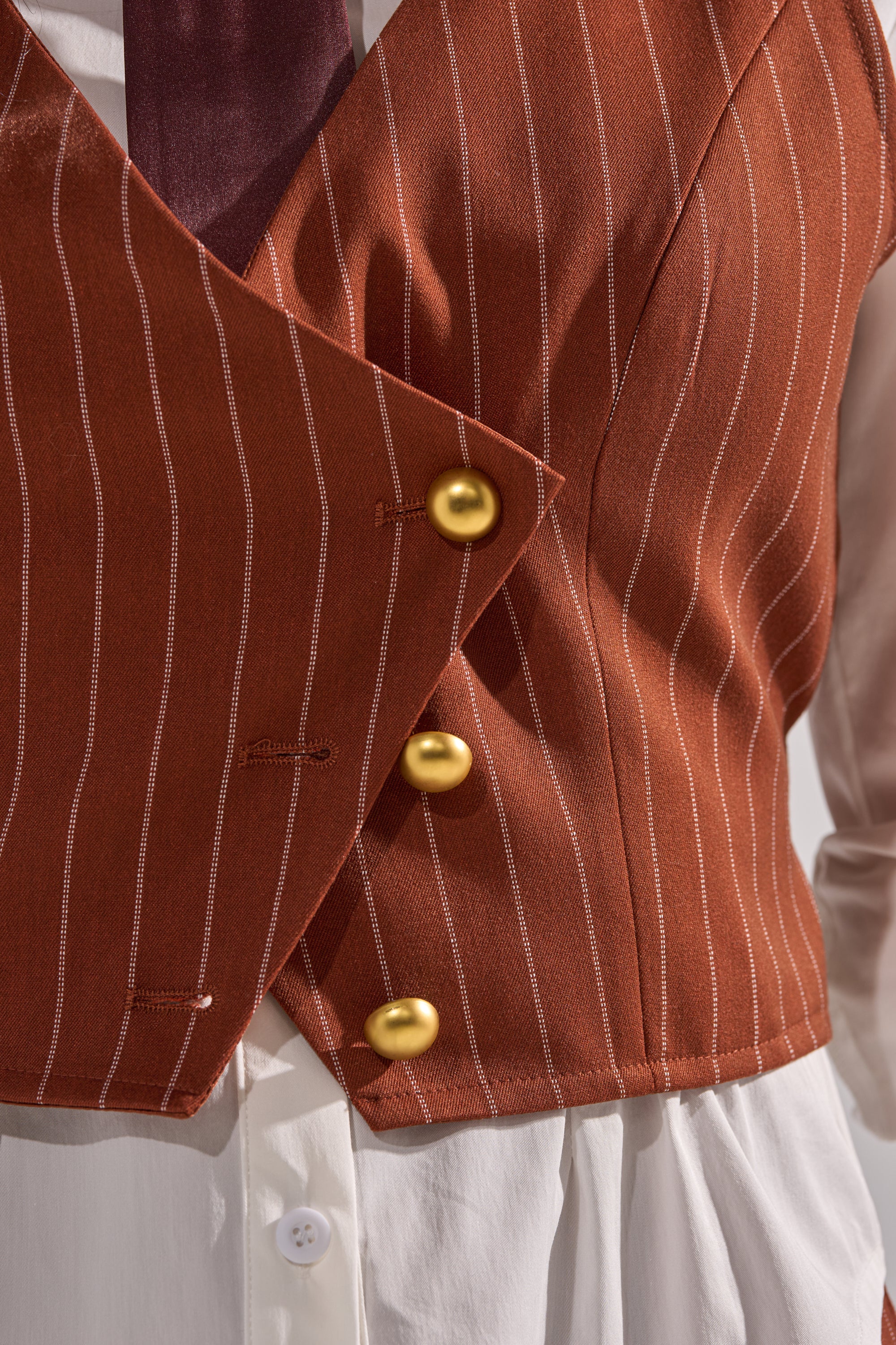 Close-up of a person wearing the BUSINESS FIRST VEST—a brown pinstripe vest with three gold buttons over a white shirt. A dark tie peeks out at the top, emphasizing this stylish business attire.