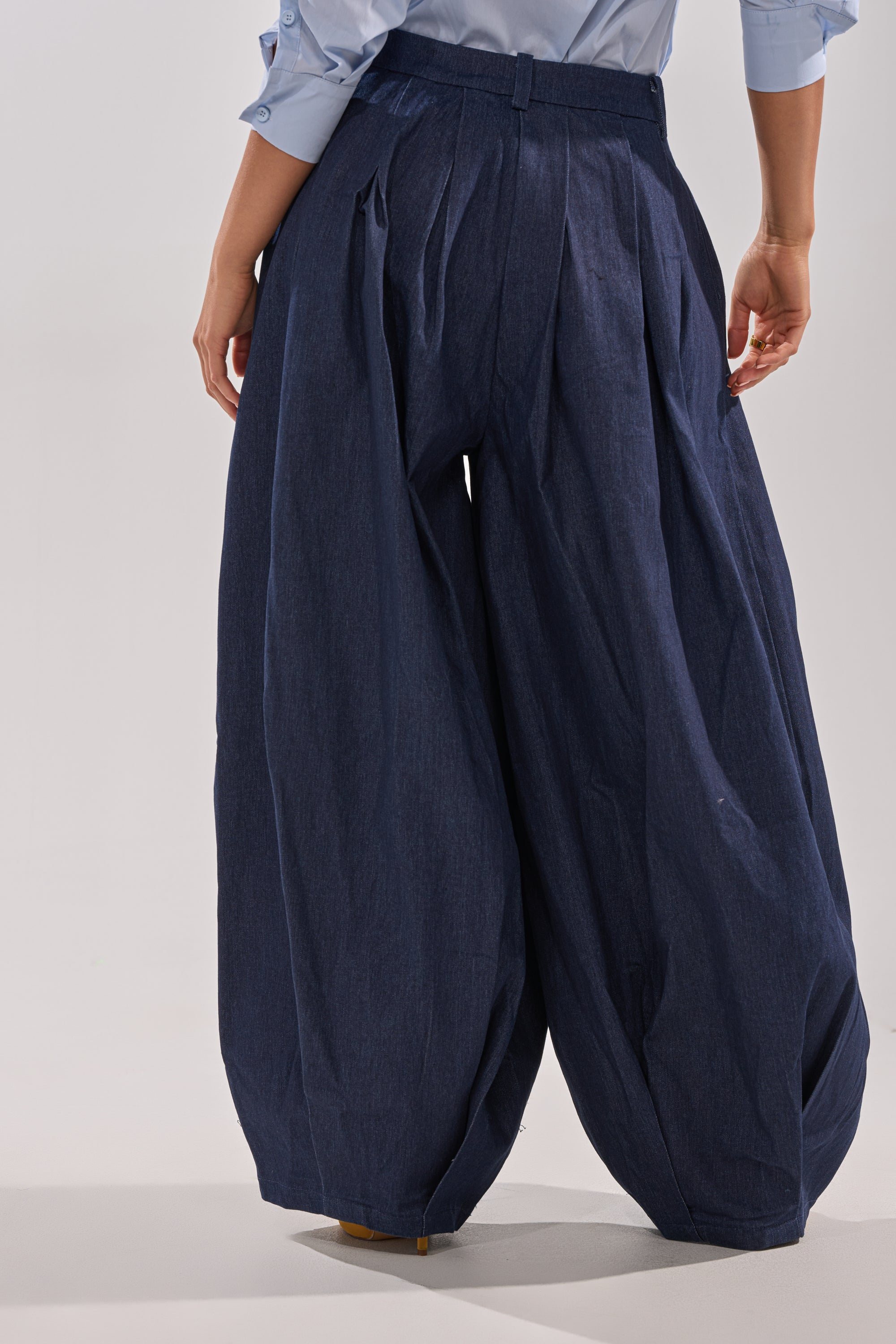 A person wears the BUSINESS IN THE FRONT TROUSER—high-rise, wide-leg navy blue pants—with a light blue shirt, standing against a plain background, shown from the waist down and viewed from behind. 7