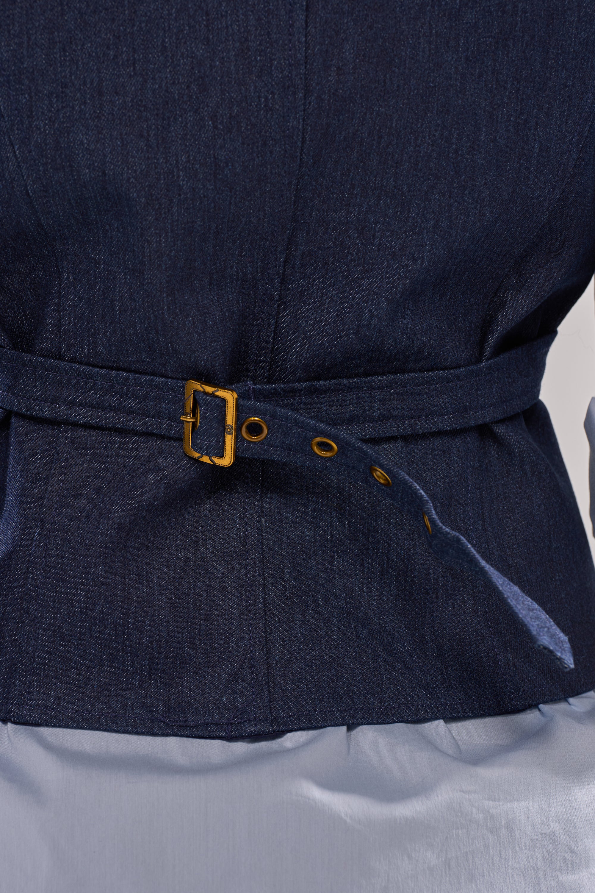 Close-up of the BUSINESS IN THE FRONT VEST in dark denim with gold hardware and belt detail, styled over a light blue shirt for a sharp, tailored look.