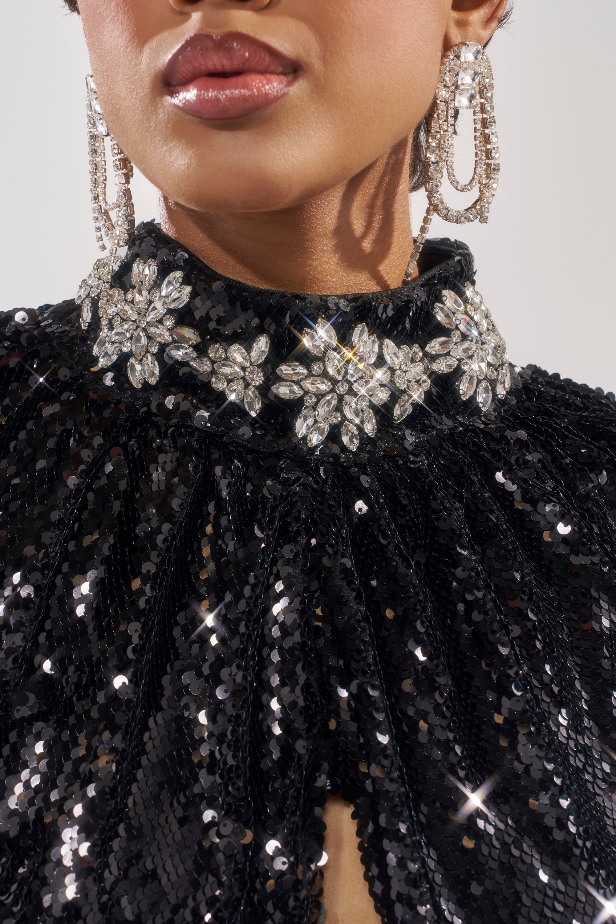 A close-up shows glossy lips and sparkling crystal earrings paired with the DAZZLING HOLIDAY SEQUIN TOP, featuring a jeweled floral collar—its light-reflecting sequins and jewels make it perfect for a festive Christmas party look.