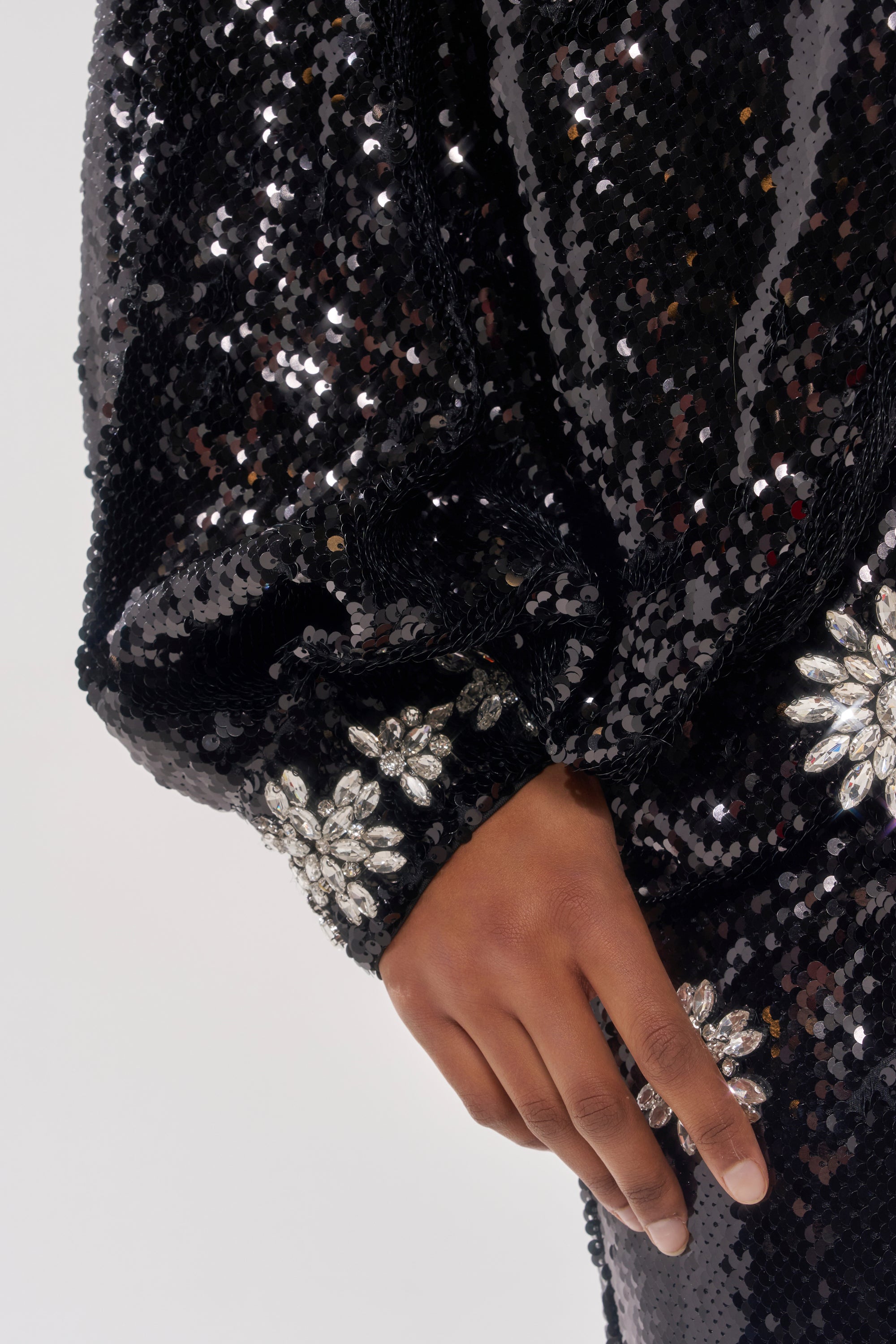 A close-up of a hand resting on the DAZZLING HOLIDAY SEQUIN TOP, featuring large silver floral embellishments near the wrist and hip.