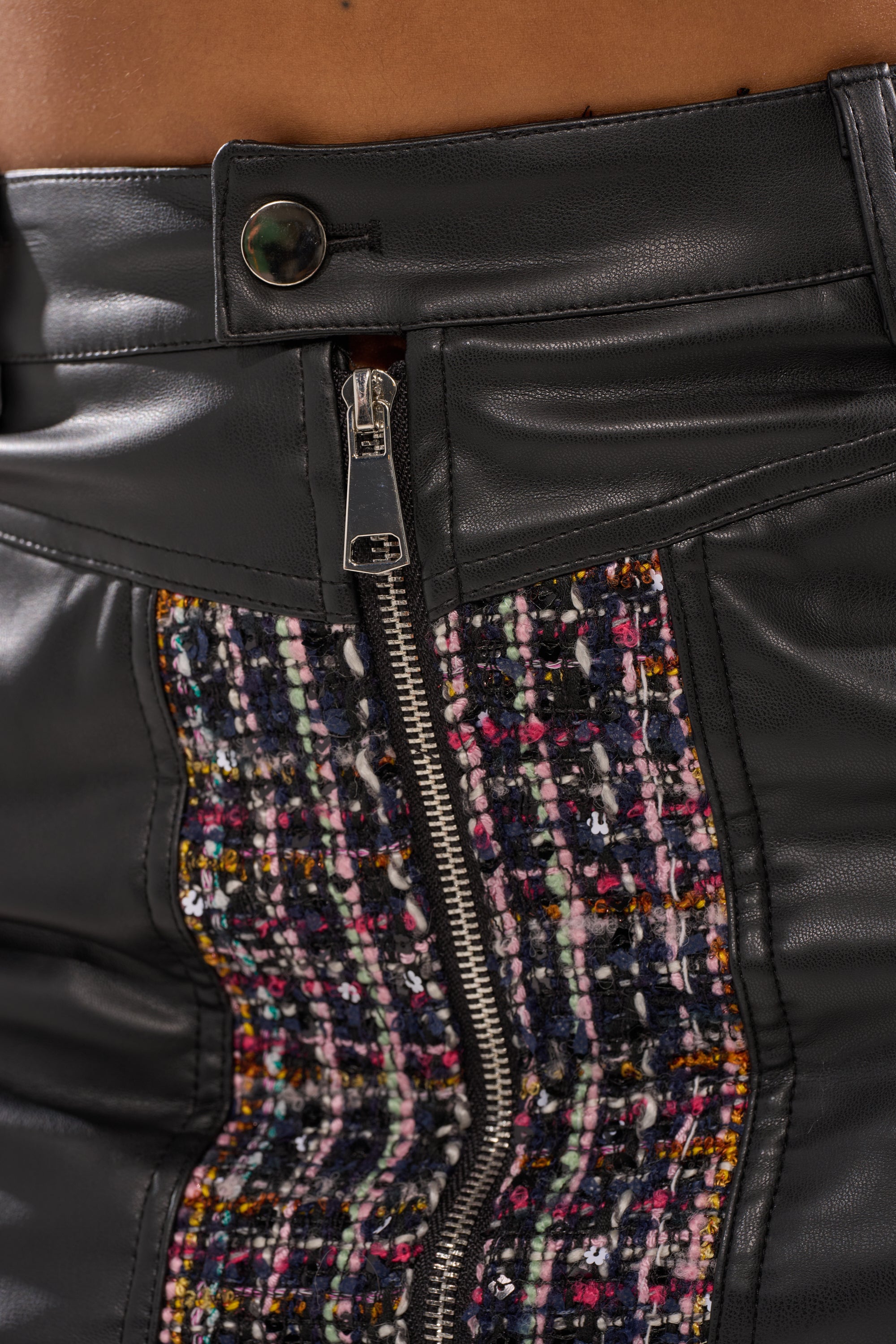Close-up of the WHAT YOU GOT FOR ME MINI SKIRT: black leather with a vertical silver zipper, central multicolored woven tweed-style panel, and a button closure waistband. 7