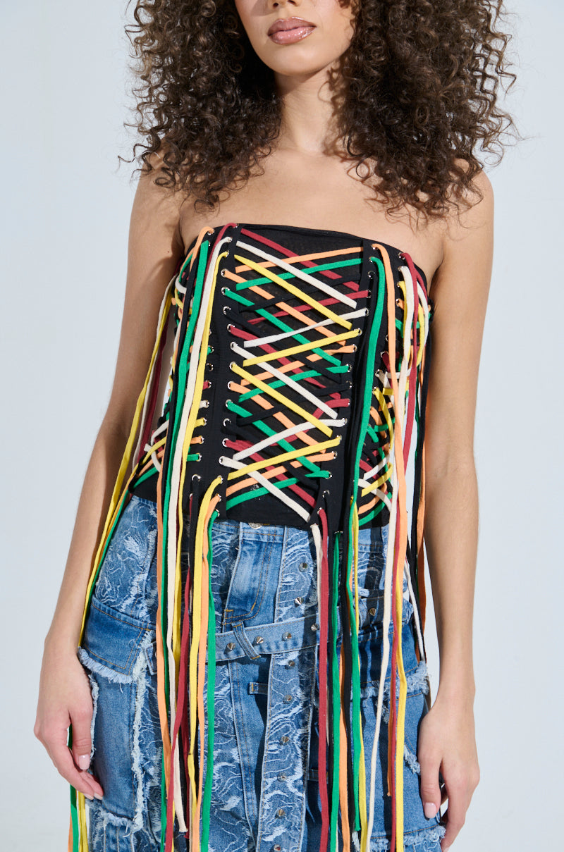 Wearing the vibrant CROSSED THE LINE CORSET with crisscrossing multicolored laces and long threads, paired with distressed blue jeans featuring patchwork designs, perfectly highlights the torso.