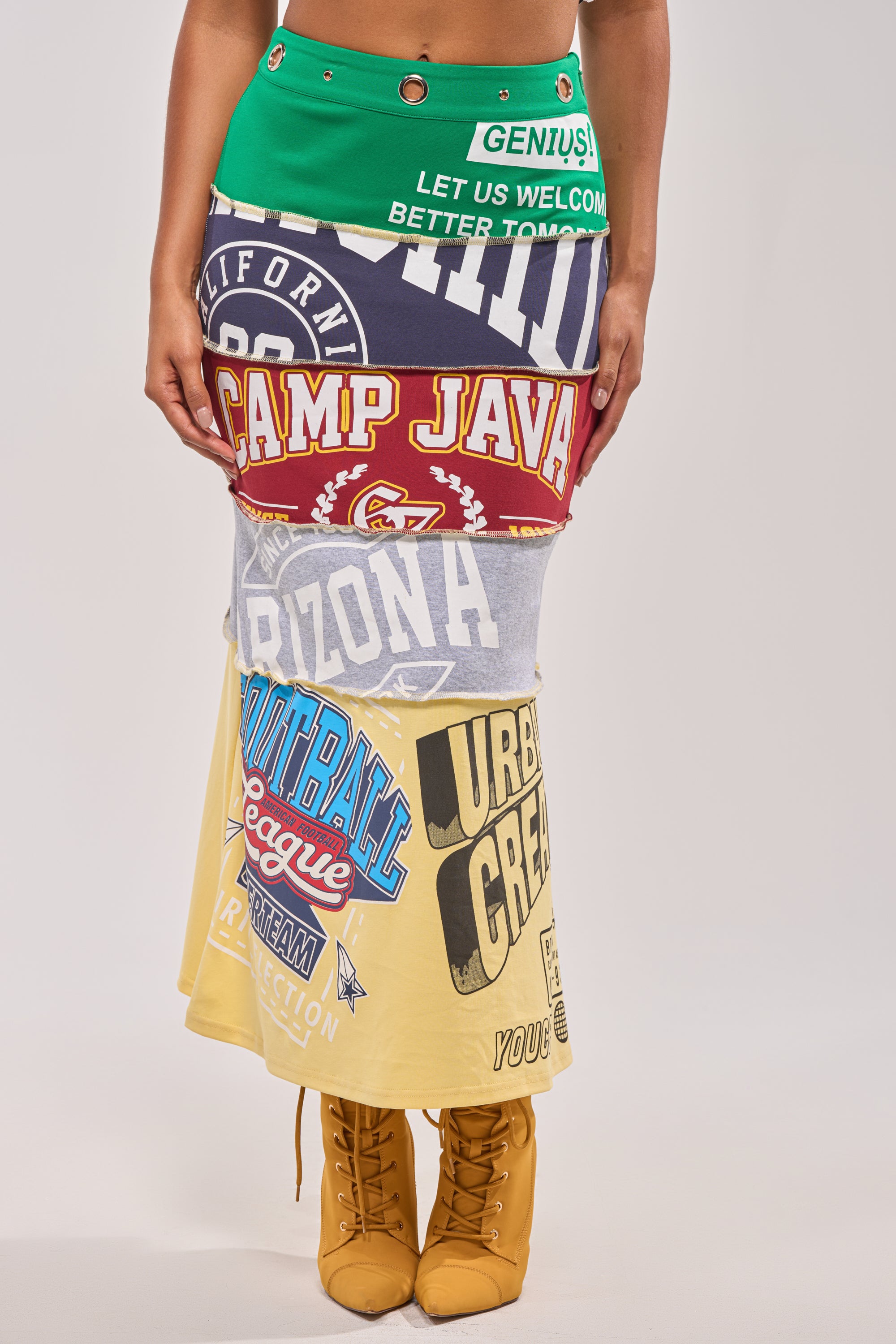 A person wears the FULL RIDE PATCHWORK MAXI SKIRT, crafted from colorful printed T-shirts, paired with yellow lace-up boots—shown waist to ankles against a plain background for bold courtside style. 1