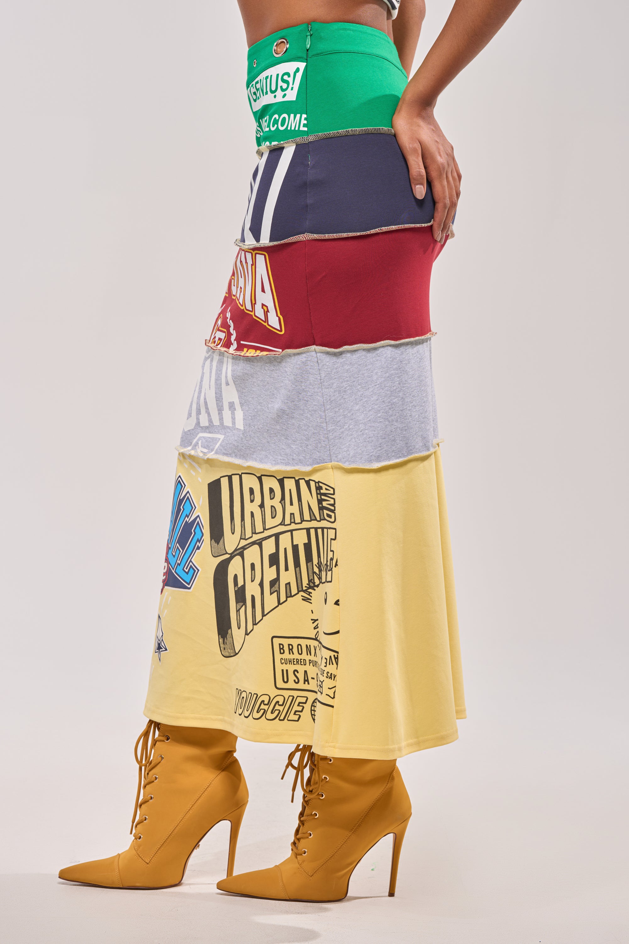 A person flaunts courtside style in the FULL RIDE PATCHWORK MAXI SKIRT, crafted from colorful T-shirts, paired with yellow high-heeled lace-up boots against a plain background. 2