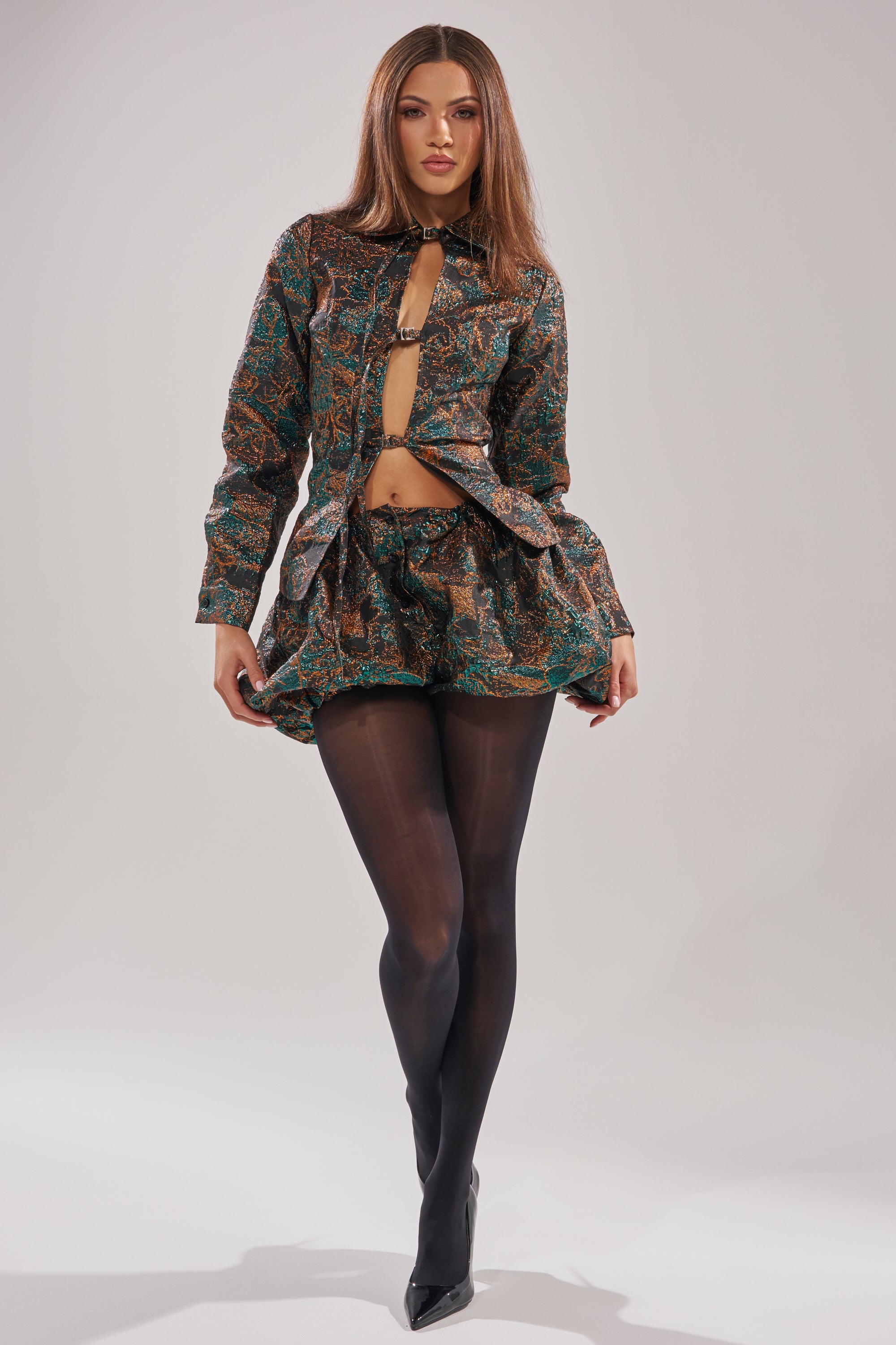 A woman poses confidently in the TOO HOT TO HANDLE BLOUSE, styled under a matching patterned jacket and mini skirt with black sheer tights and pointed heels, set against a plain light background. 5