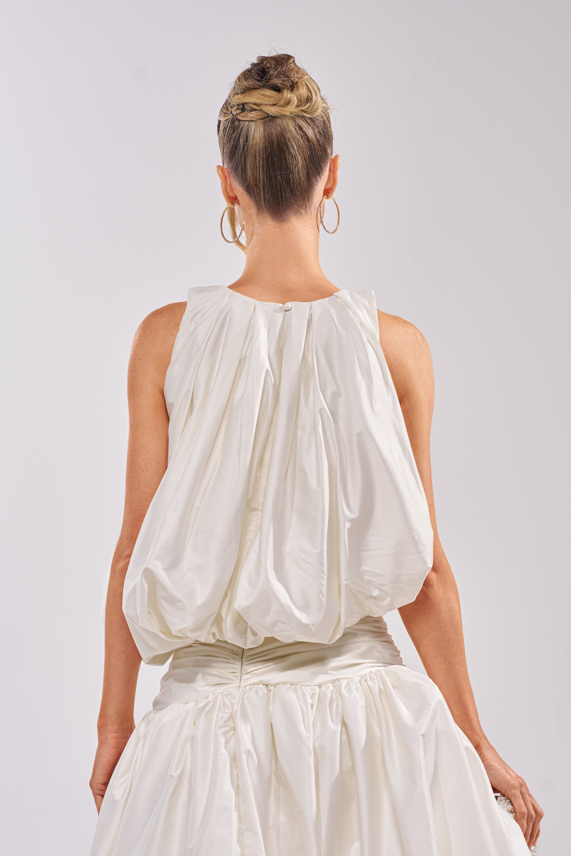 A woman with braided hair in a bun and large hoop earrings is shown from the back against a plain light background, wearing the HEAD IN THE CLOUDS SLEEVELESS BLOUSE. 3