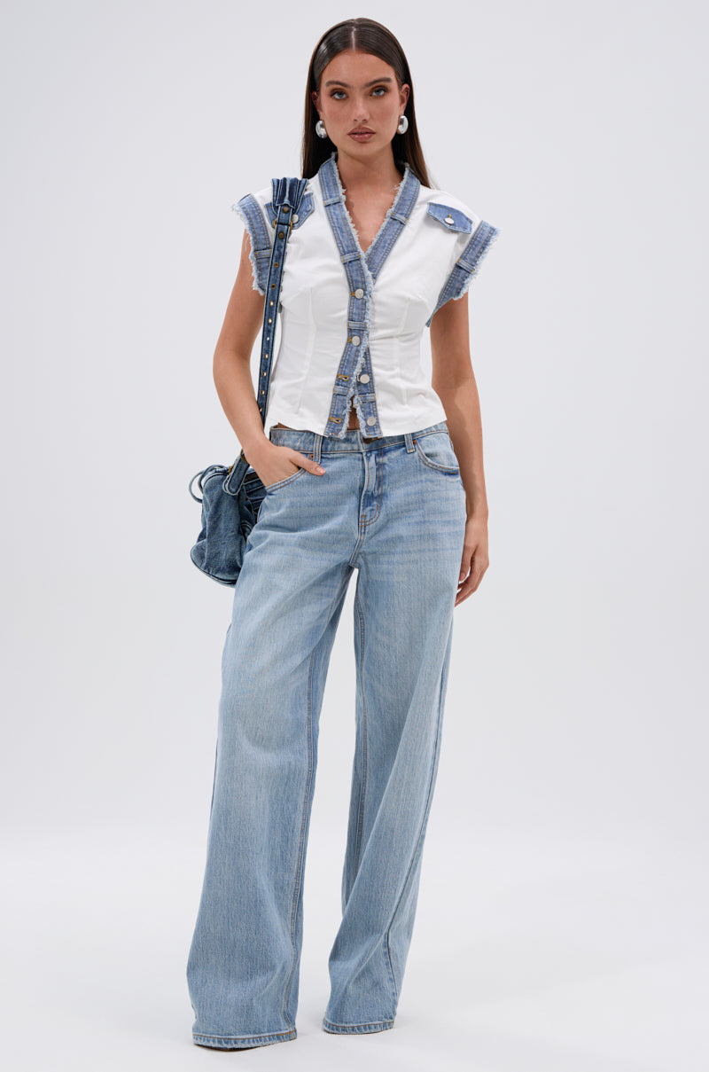 A woman with long brown hair wears the DENIM BABY BUTTON DOWN TOP with denim trim, paired with wide-leg light blue jeans, a matching denim shoulder bag, and earrings—creating a street-style summer look against a plain background. 5