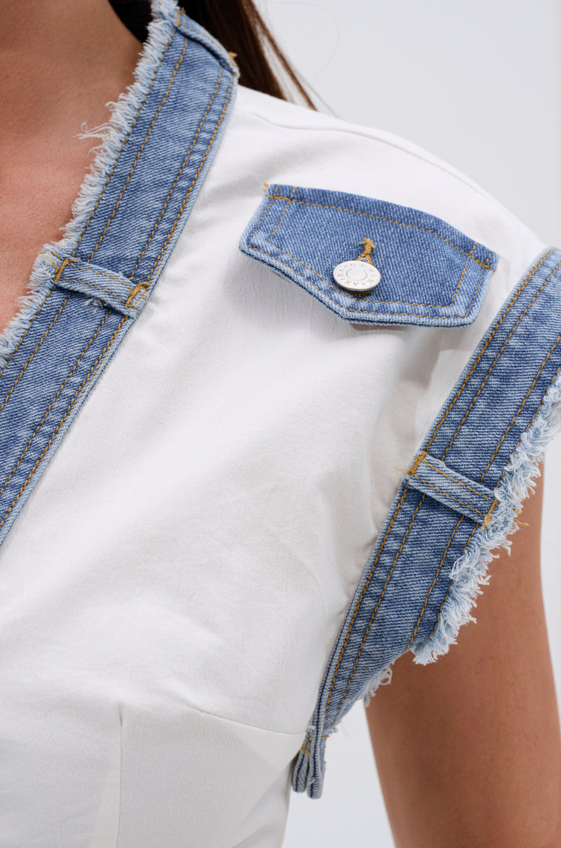 Close-up of a person in the DENIM BABY BUTTON DOWN TOP, showing frayed denim trim at the sleeve, shoulder, and flap with a silver button—an effortlessly cool summer piece. Only part of their upper chest, shoulder, and arm are visible. 7