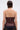 A person with short, slicked-back hair is seen from behind wearing the WHATEVER SHE WANT FAUX LEATHER CORSET in dark burgundy with a back zipper, paired with dark denim pants against a plain light gray background.