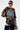 A woman in oversized sunglasses, the OFF TO THE RACES DISTRESSED OVERSIZED TEE, metallic leggings, furry black leg warmers, and holding a small multicolored bag stands against a plain white background.