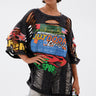A woman in oversized sunglasses, the OFF TO THE RACES DISTRESSED OVERSIZED TEE, metallic leggings, furry black leg warmers, and holding a small multicolored bag stands against a plain white background.