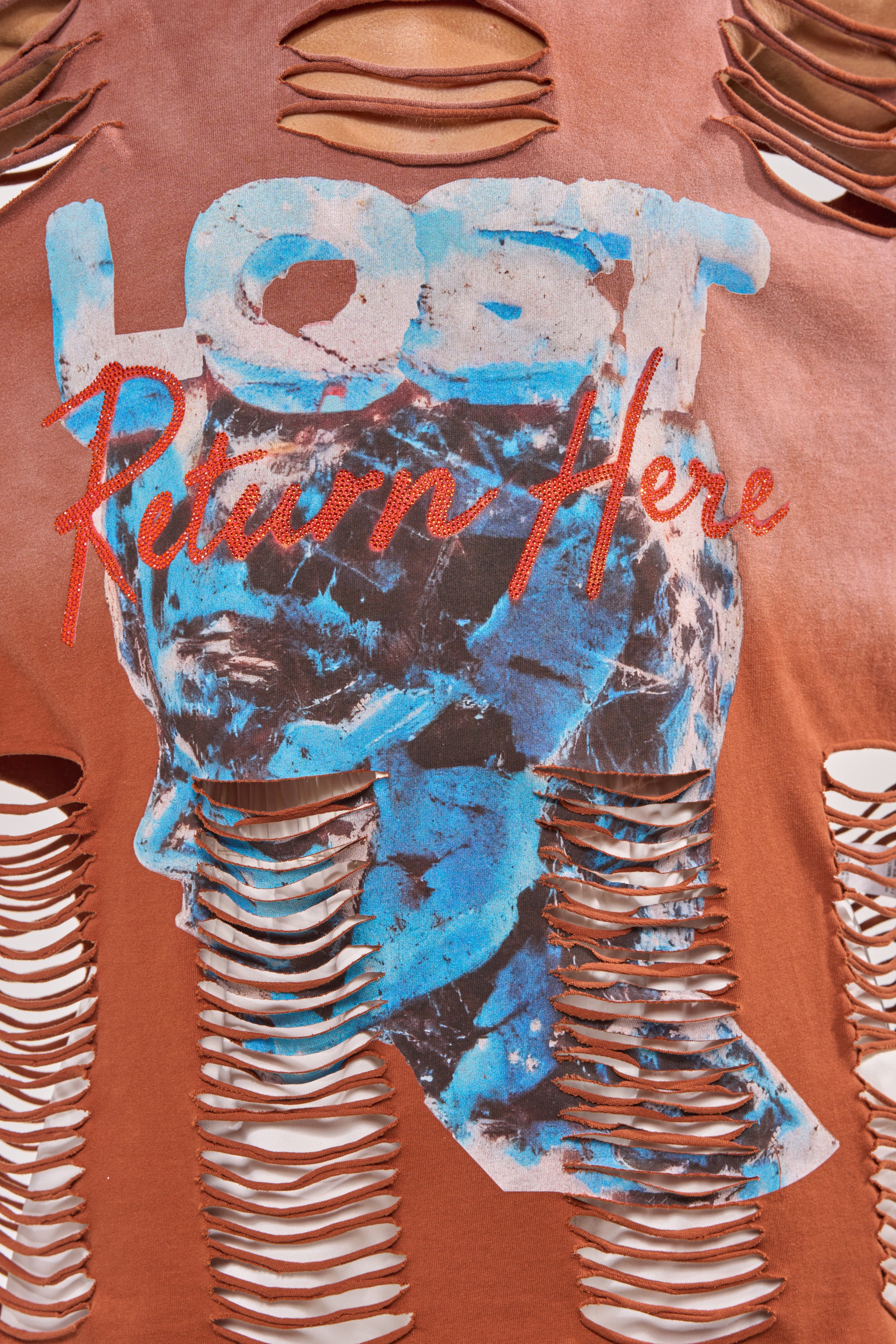 The BYE GIRL OVERSIZED DISTRESSED TEE IN BROWN is a streetwear shirt with "LOST" in blue and white, "Return Here" in red cursive, and an abstract blue human head graphic on a distressed brown background. 6