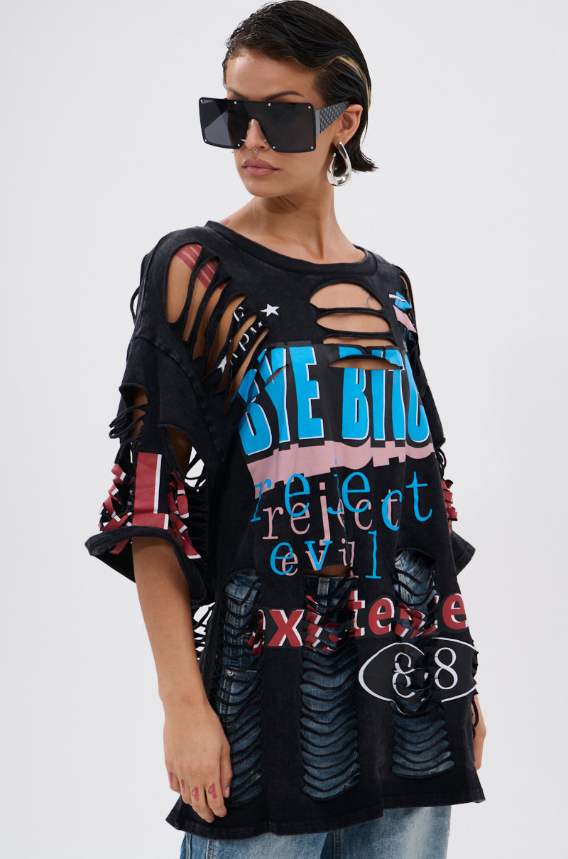 A woman in large black sunglasses and the BYE GIRL OVERSIZED DISTRESSED TEE, featuring colorful graphic text and ripped details, stands against a white background for a bold, statement-making look. 0