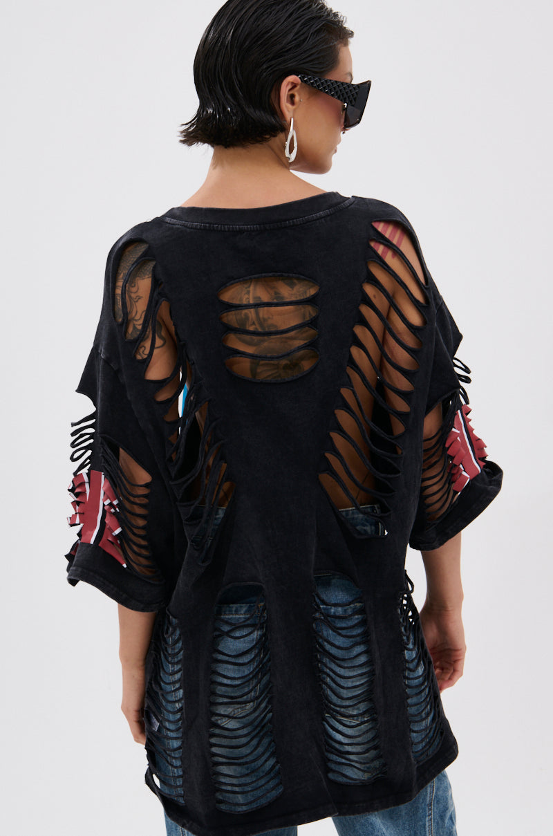 Wearing the BYE GIRL OVERSIZED DISTRESSED TEE, a person with short, wet-look hair and sunglasses reveals back and arm tattoos. Paired with blue jeans, they're photographed from behind against a plain background. 3
