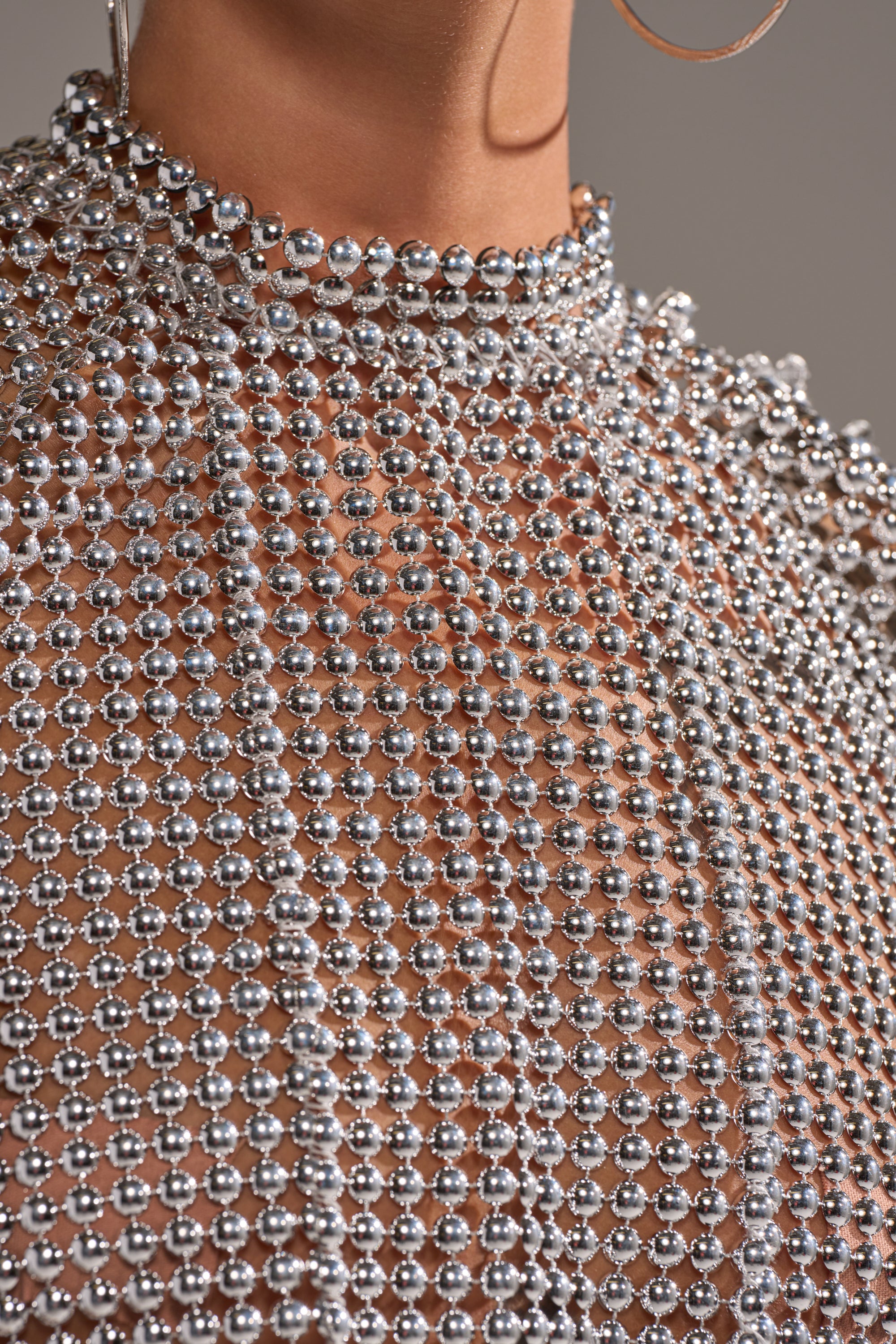 Close-up of a person wearing the BEADS FOR DAYS TEE—a silver, high-neck top adorned with shiny beads in intricate mesh patterns for a sparkling and luxurious look. 8