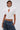 A woman poses confidently in the TOO COOL FOR YOU LACEUP BLOUSE—a fitted white puff sleeve top with a high collar and keyhole cut-out—paired with loose blue jeans. Her short, slicked-back hair adds to the modern look against a plain background.